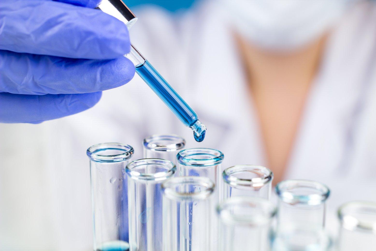 Sientist with pipette blue water drop in test tubes in laboratory.